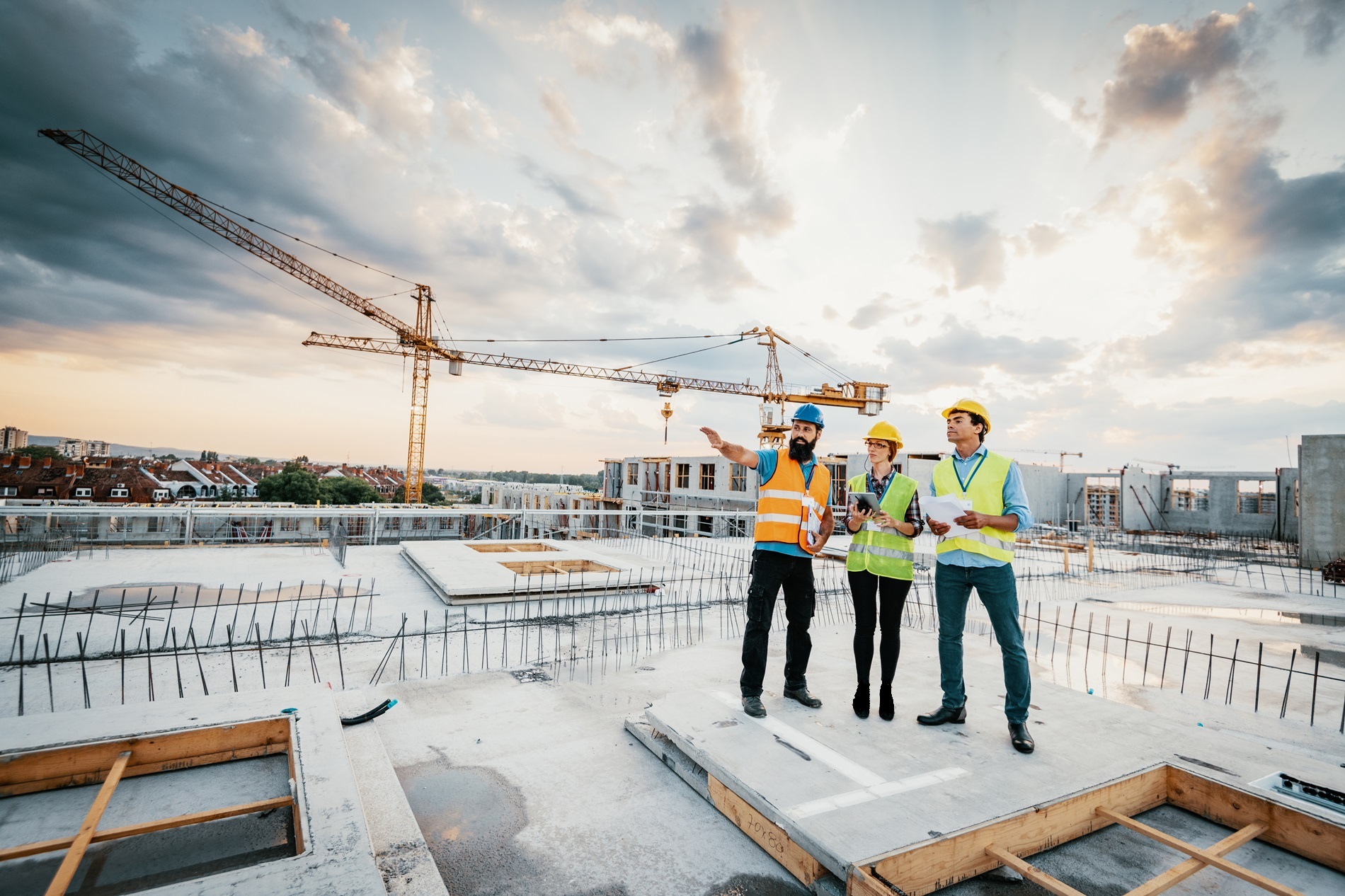 Construction management team wearing safety gear on a construction site with cranes in background