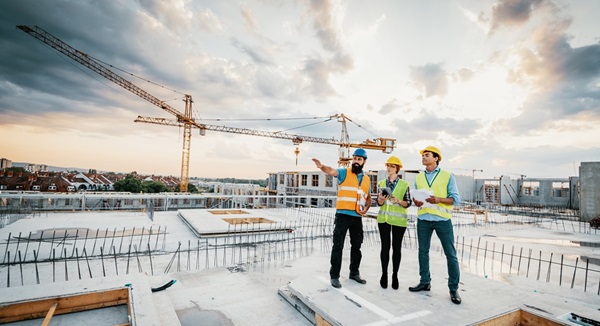 Construction management team wearing safety gear on a construction site with cranes in background