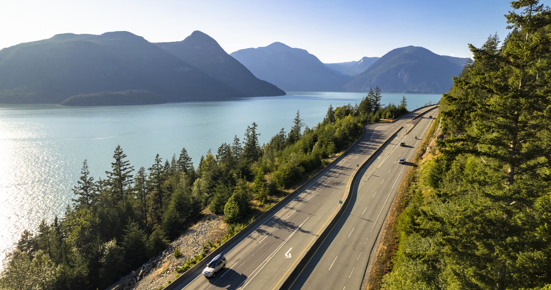 Multiple cars driving highway alongside the ocean and mountains in BC 