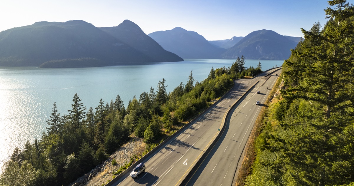 Multiple cars driving highway alongside the ocean and mountains in BC 