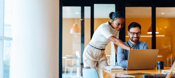 Black female with haired pulled back assisting her male colleague on the computer.