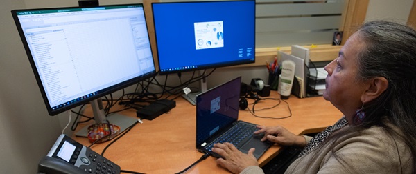 Indigenous female at her desk working on her laptop with multiple screens