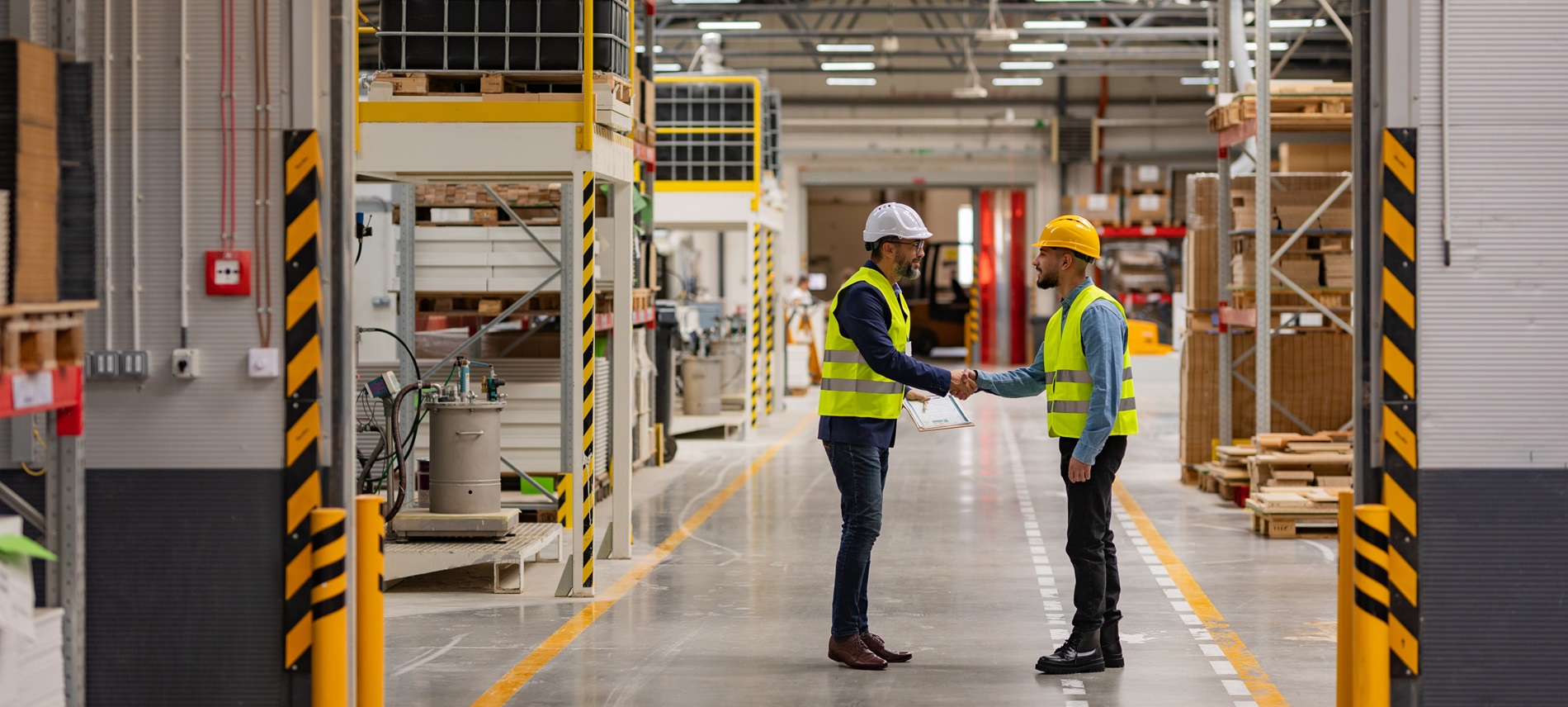 Male supervisor shaking hand of new employee on warehouse floor, both wearing safety gear
