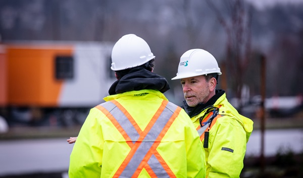 Two male employees wearing safety gear talking outdoors