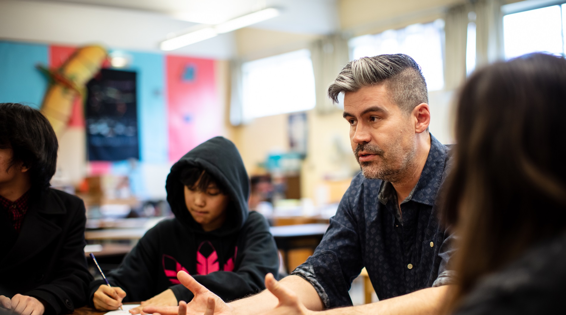 Male teacher sitting at table with students having a discussion 