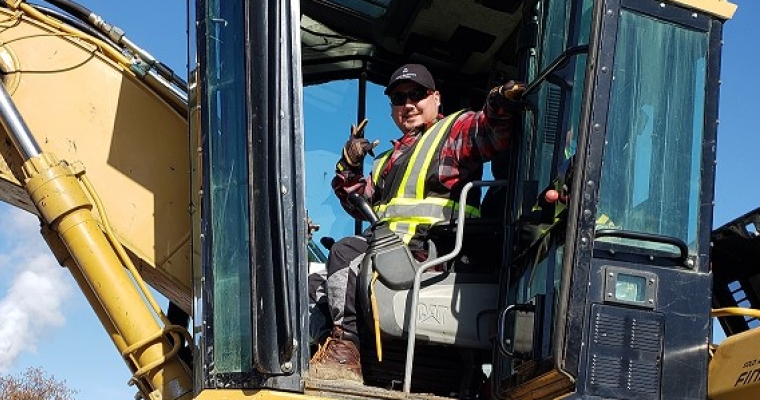 Darryl sits on a construction site inside his heavy equipment.