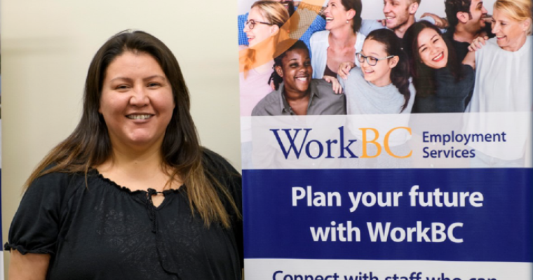 Rhonda stands happily in front of banner for WorkBC services.