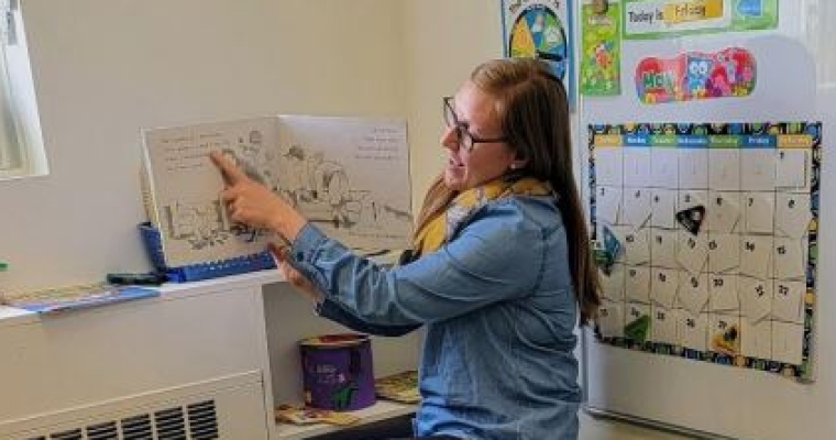 Samantha reads a book to children in daycare.