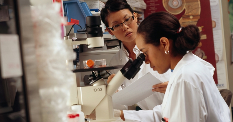 Female teacher instructing a female student on using a microscope