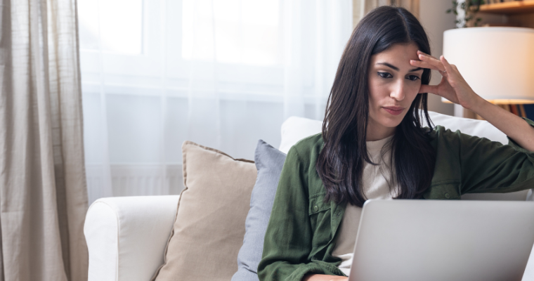 woman sitting on couch looking at laptop screen with worried expression