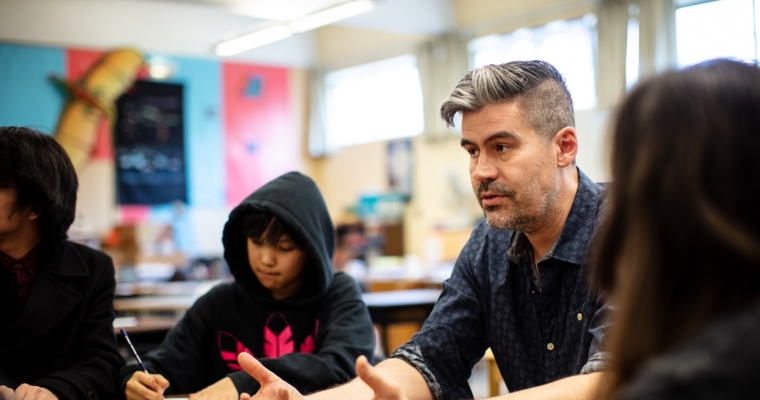 Male teacher sitting at table with students having a discussion 