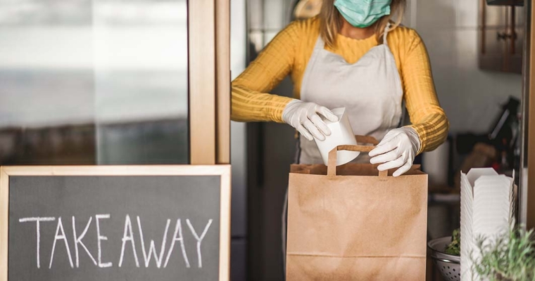 employee wearing mask and gloves packing food at takeaway counter