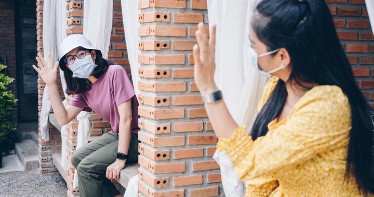 two women wearing masks waving to each other from separate window panes
