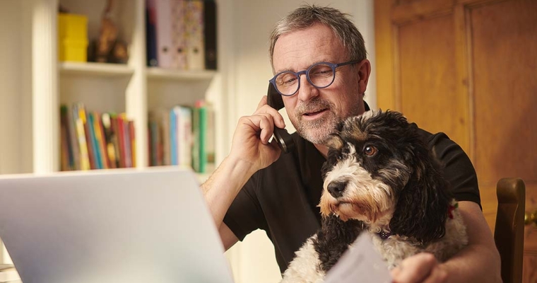 man on phone working in home office with his dog on his lap