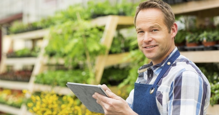 man wearing apron and holding clipboard standing in front of plants