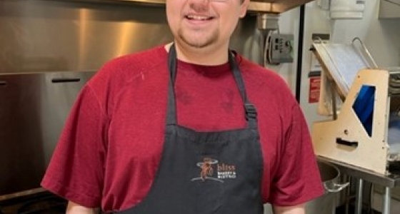 Trenton smiles in kitchen of his new job wearing an apron.