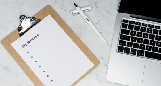 A resume on a clipboard rests next to a laptop computer