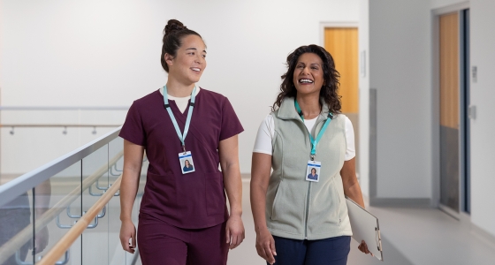 A pair of smiling female health-care workers walking together down the hall of a hospital.