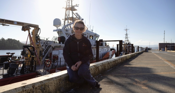 oceanographer sitting at worksite with ship behind her