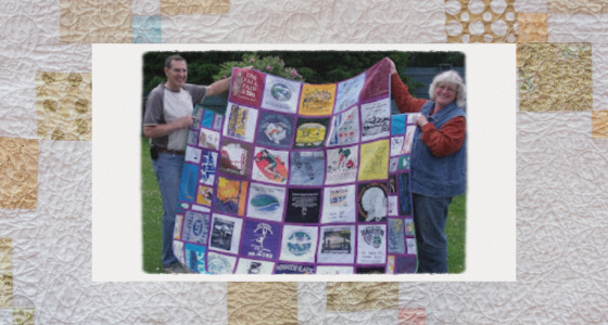 Caroline and a man holding up one of her quilts