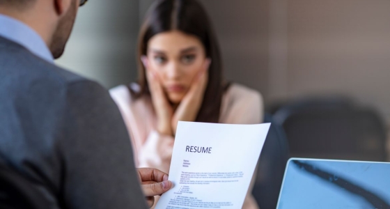 Hiring manager reads over resume as a nervous young job applicant looks on during interview in office