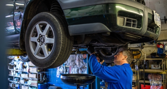 man in overalls repairing a car that is raised on a hoist