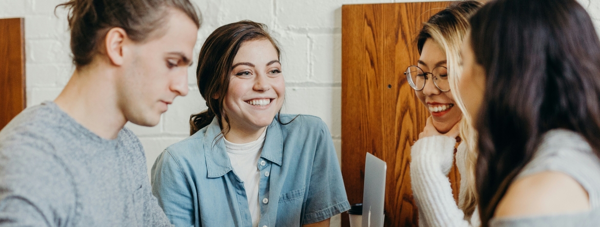 group of four people smiling and talking while holding coffees and electronic devices