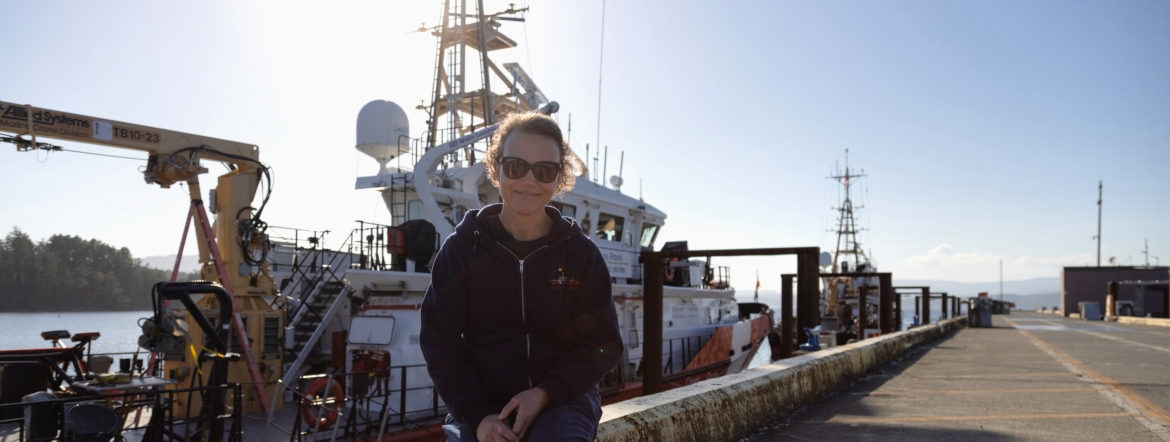 oceanographer sitting at worksite with ship behind her