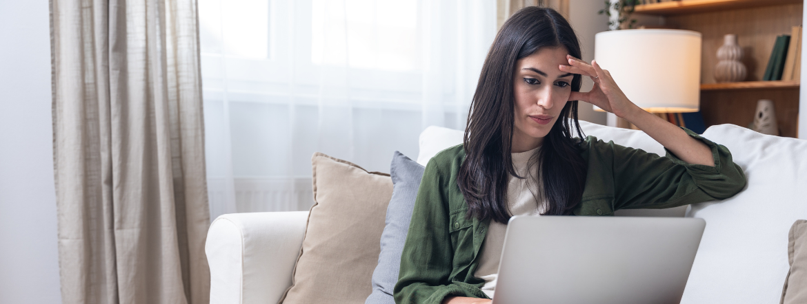 woman sitting on couch looking at laptop screen with worried expression