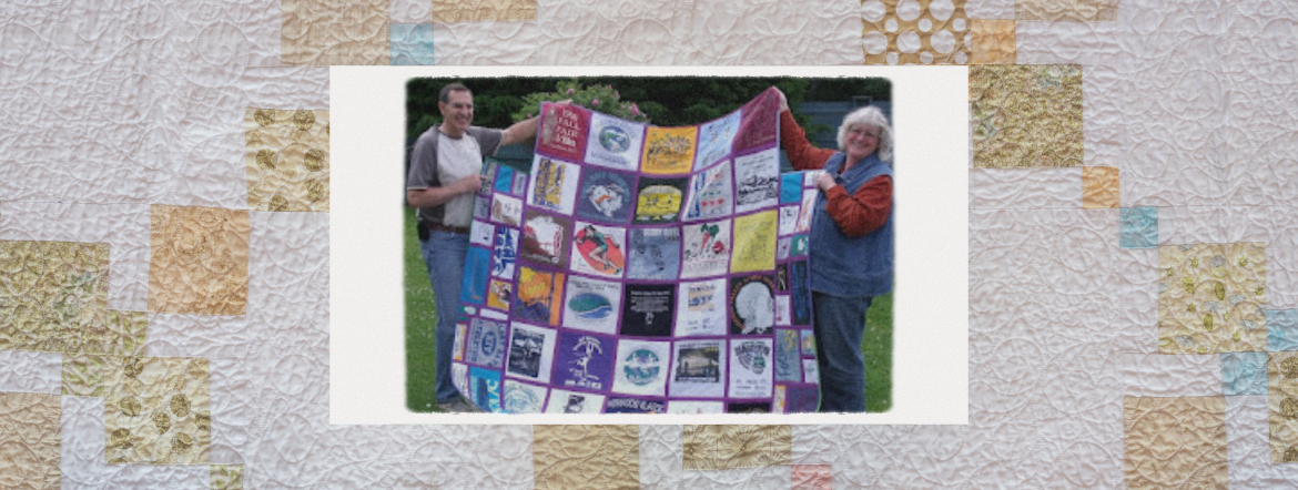 Caroline and a man holding up one of her quilts
