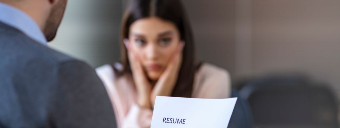 Hiring manager reads over resume as a nervous young job applicant looks on during interview in office