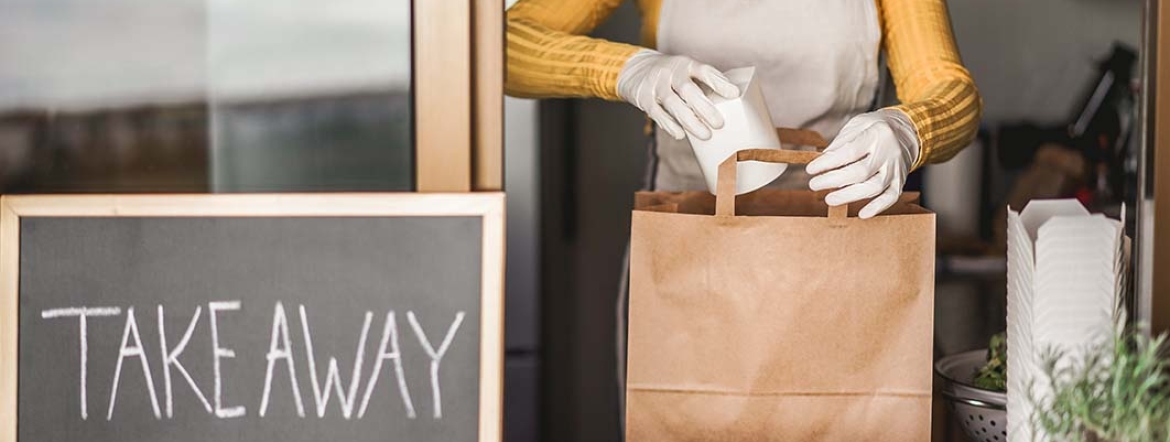 employee wearing mask and gloves packing food at takeaway counter
