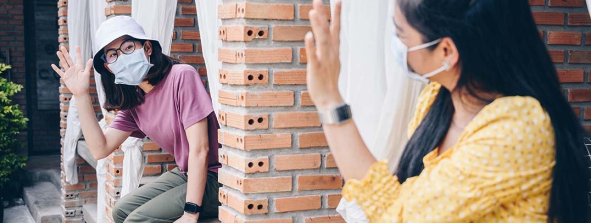 two women wearing masks waving to each other from separate window panes