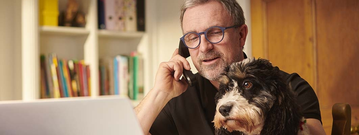 man on phone working in home office with his dog on his lap