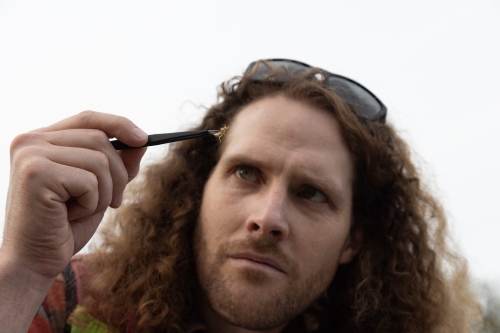 Aaron holding an insect sample up with tweezers and inspecting it.