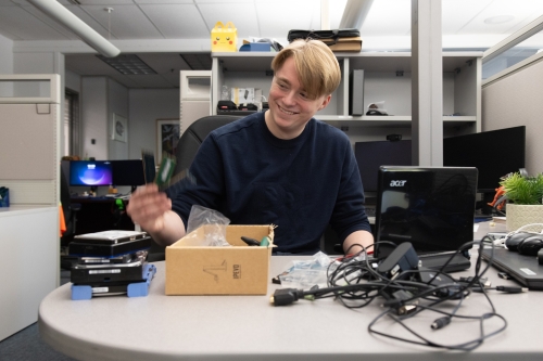 Hawkeye sitting at his desk and smiling as he works with computer components.