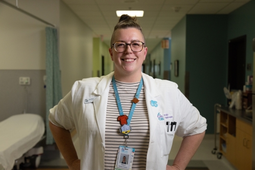 Kaitlyn wearing a lab coat in a hospital while smiling at the camera.