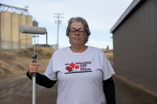 Karla standing and holding a paint roller at a work site.