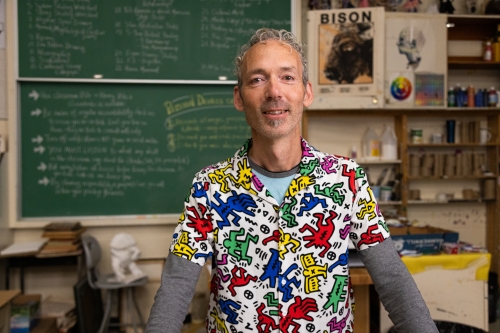 Perry standing in his art classroom wearing a brightly coloured shirt.