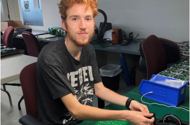 Lucas faces camera while seated in front of technical equipment at his new job.