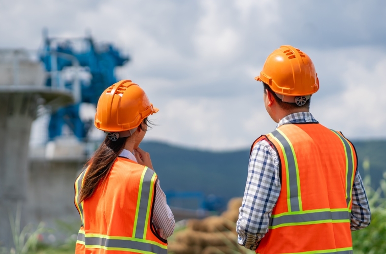 One female and one male construction worker overlooking a construction site.