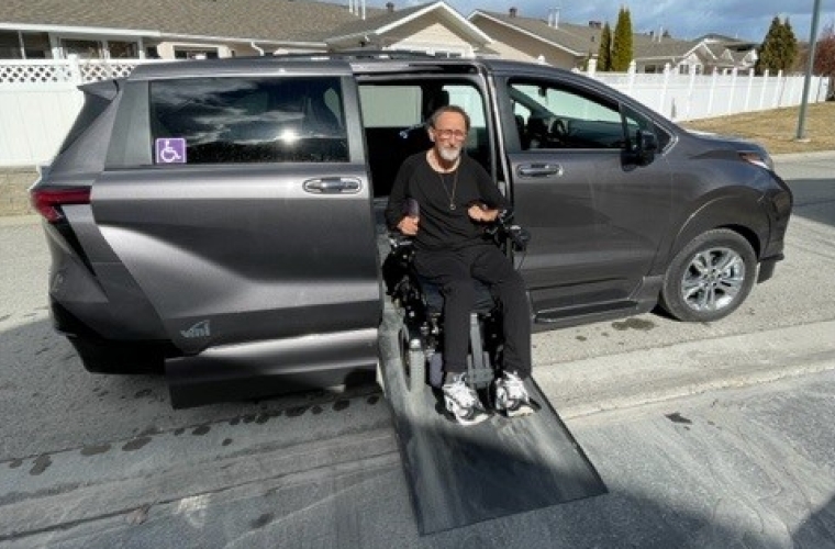 An older man exiting from the side door of a van in a wheelchair using a ramp