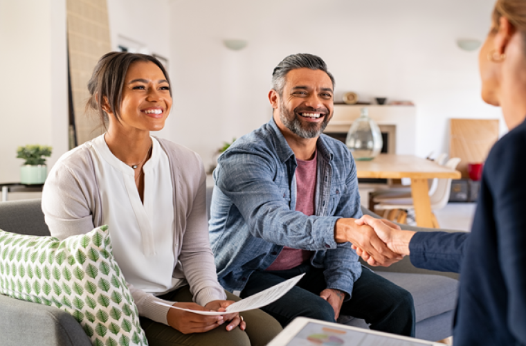 Multiethnic couple handshake with financial advisor at home.