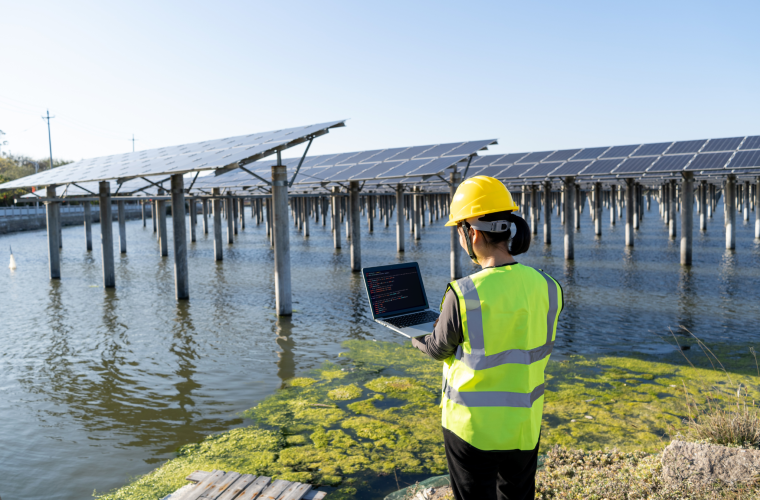 Asian female engineer wearing safety helmet and vest using laptop at solar power plant