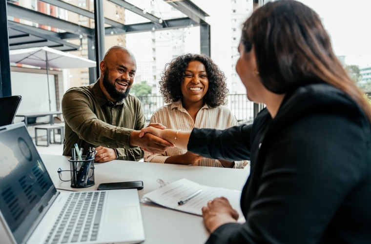 Black couple shaking hands with a financial advisor with computer over a document