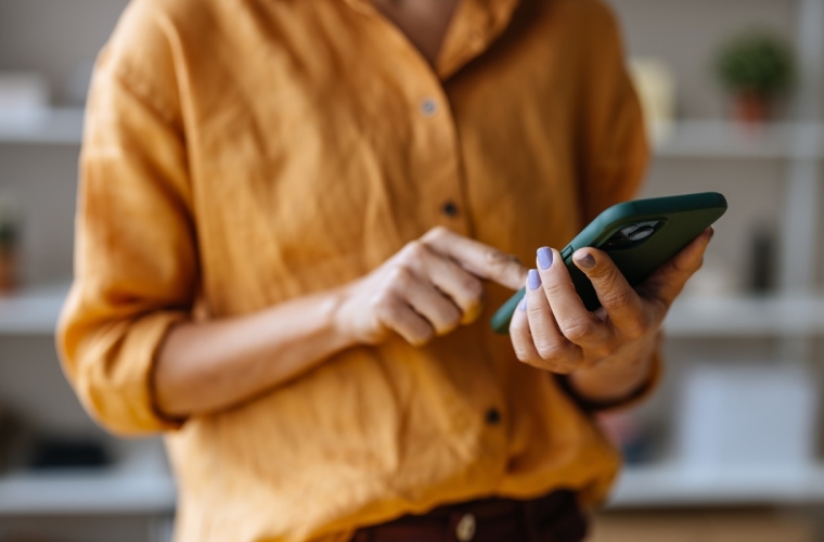 female body wearing an orange shirt while scrolling her on green cellphone.