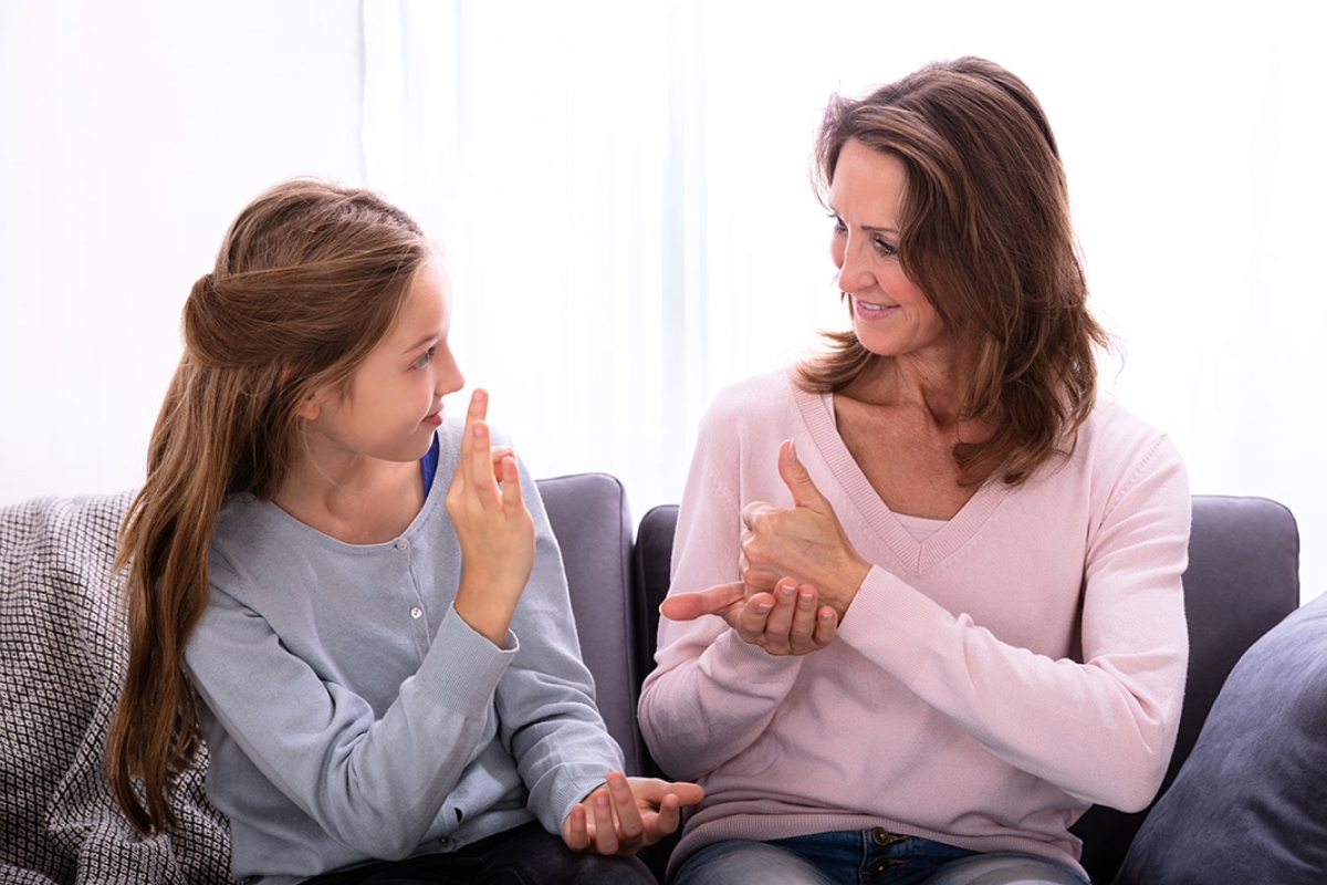 mother and daughter sitting on couch using sign language