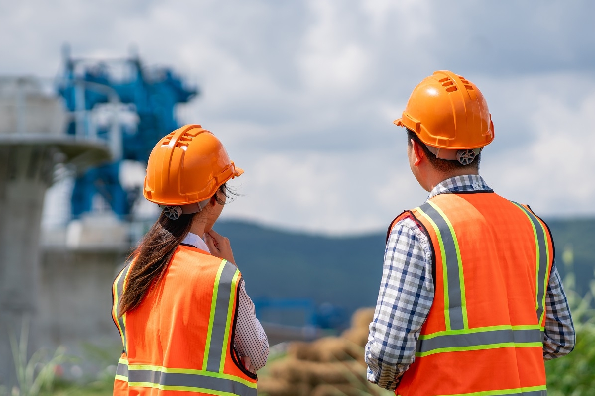 One female and one male construction worker overlooking a construction site.