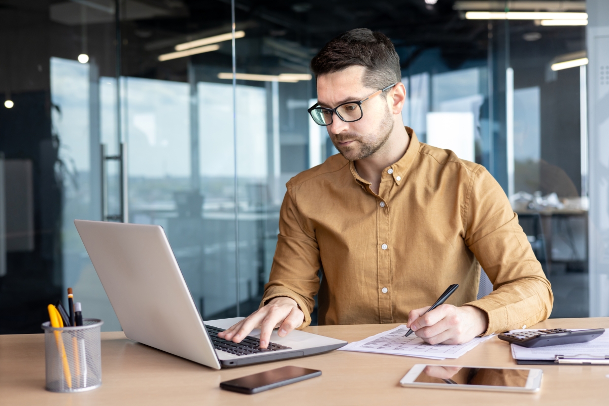 Young male accountant works in the office with laptop and financial documents. 