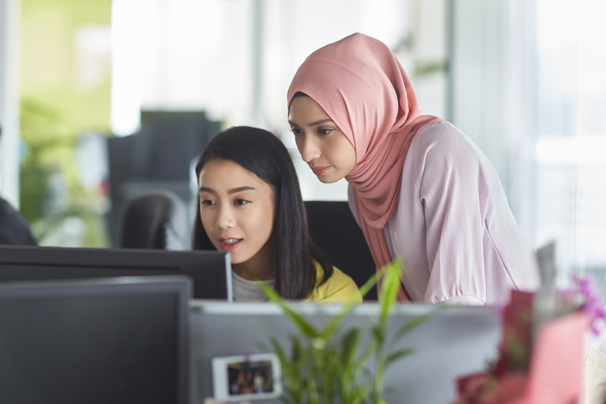 Diverse female colleagues looking at computer in office.